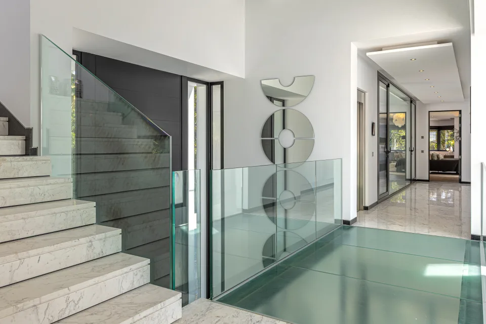 Fotografía de interiorismo y arquitectura de un elegante vestíbulo con escalera de mármol y barandilla de vidrio en Guadalmina Baja