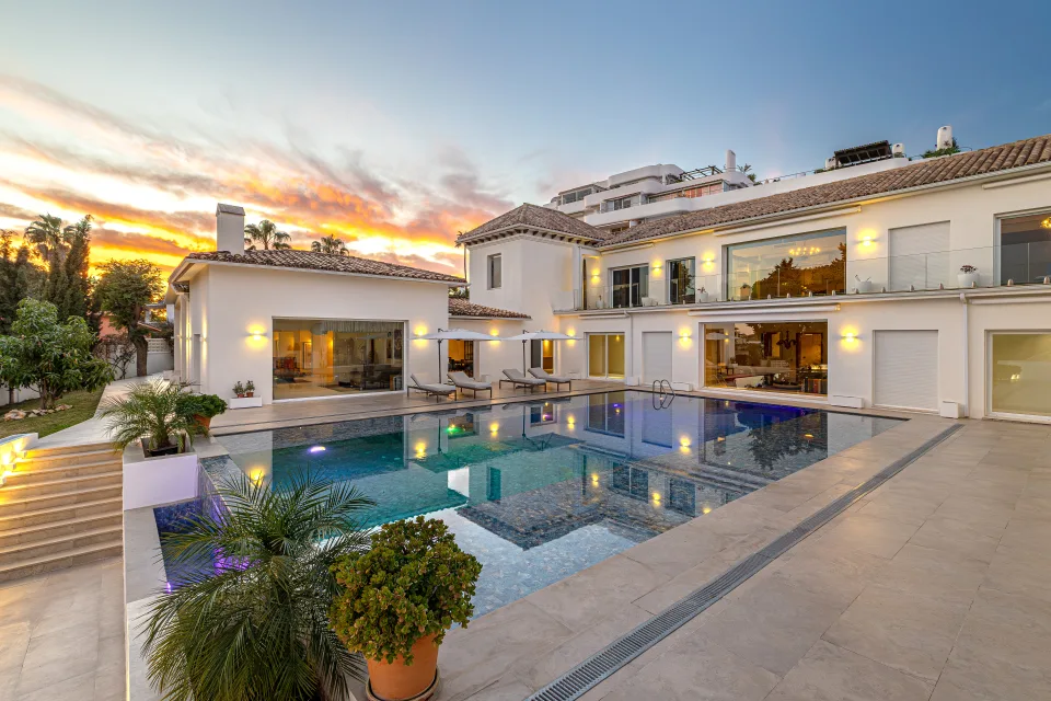 Real estate photograph of an elegant villa with an outdoor pool surrounded by gardens and large windows in Marbella