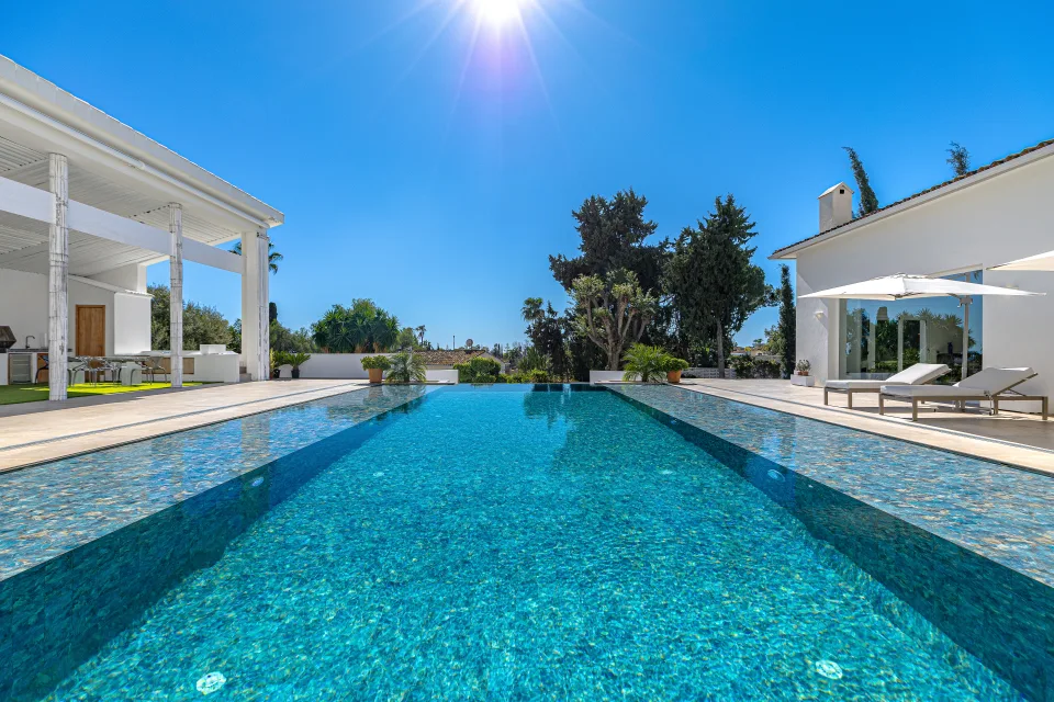 Real estate photograph of an elegant infinity pool surrounded by well-maintained gardens and sun lounge in Marbella