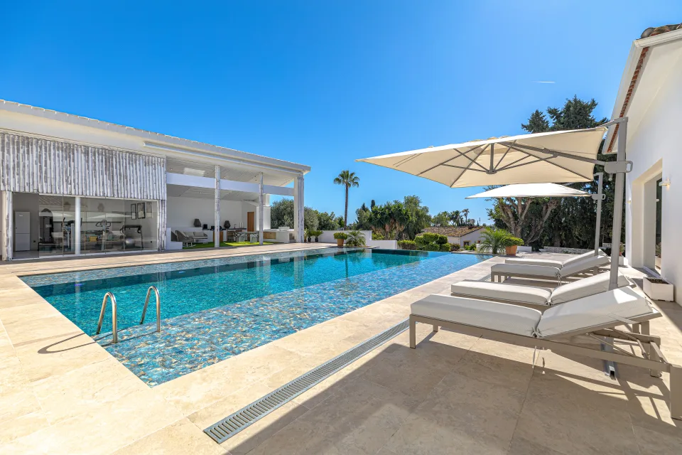 Real estate photograph of a stylish villa with infinity pool and sun loungers by a sunny garden in Marbella