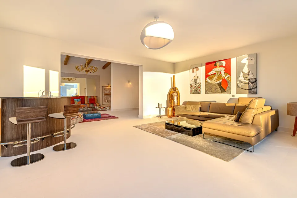 Real estate photograph of a bright living room with leather sofa, bar counter, and artworks on the walls in Marbella