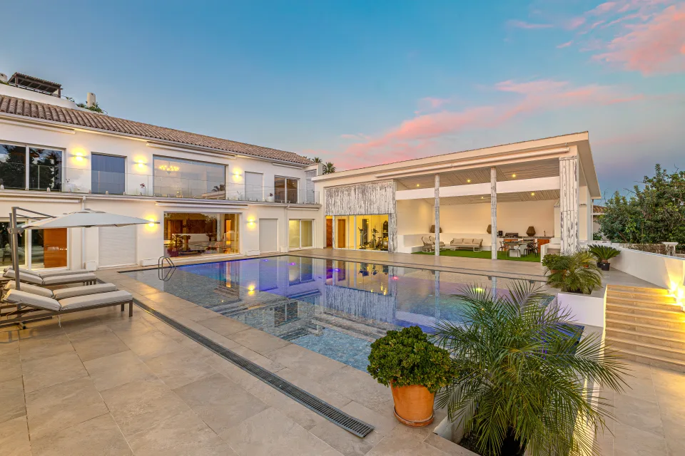 Fotografía inmobiliaria de una villa moderna con piscina desbordante, amplias terrazas y ambiente acogedor al atardecer en Marbella