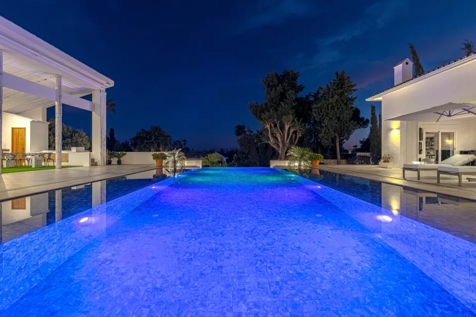Fotografía inmobiliaria de una elegante piscina iluminada con luces de colores, rodeada de vegetación en Marbella