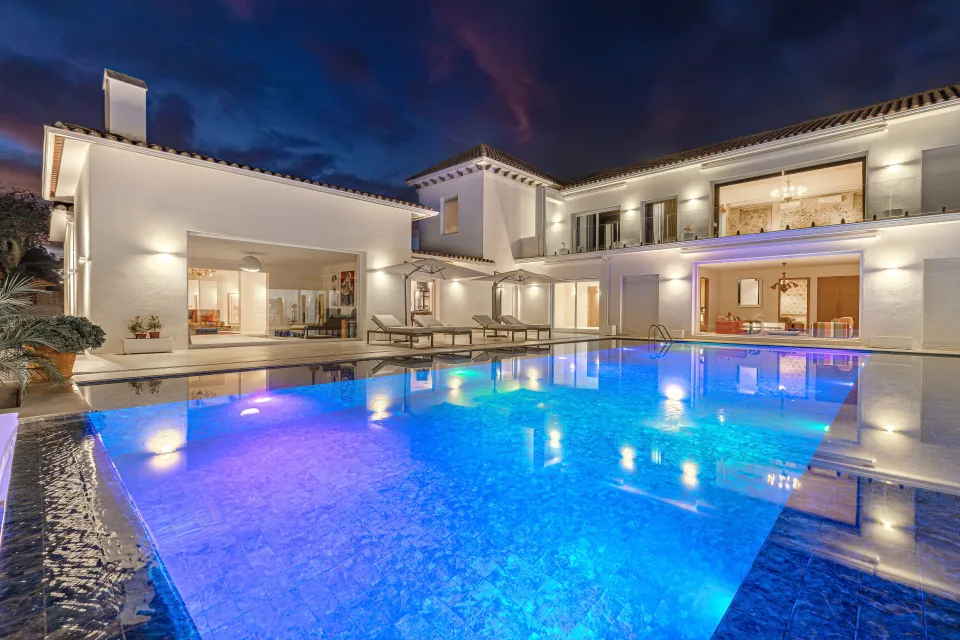Fotografía inmobiliaria de una villa con piscina iluminada, amplias terrazas y elegantes detalles arquitectónicos en Marbella