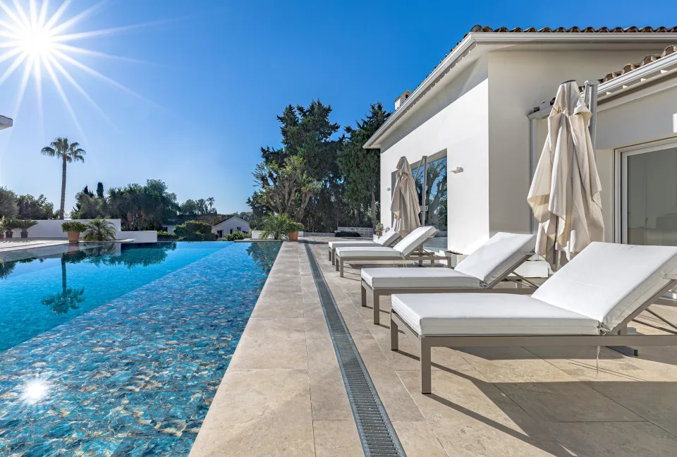 Fotografía inmobiliaria de una elegante piscina con tumbonas blancas y vistas al jardín en Marbella