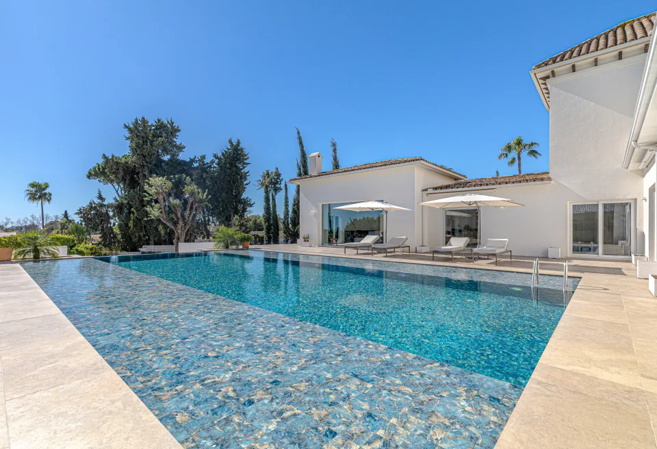 Fotografía inmobiliaria de una villa moderna con piscina de agua cristalina rodeada de jardín en Marbella