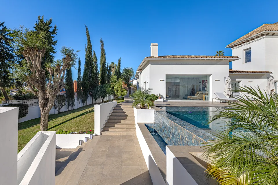 Fotografía inmobiliaria de un jardín bien cuidado con piscina y camino adoquinado hacia la villa en Marbella