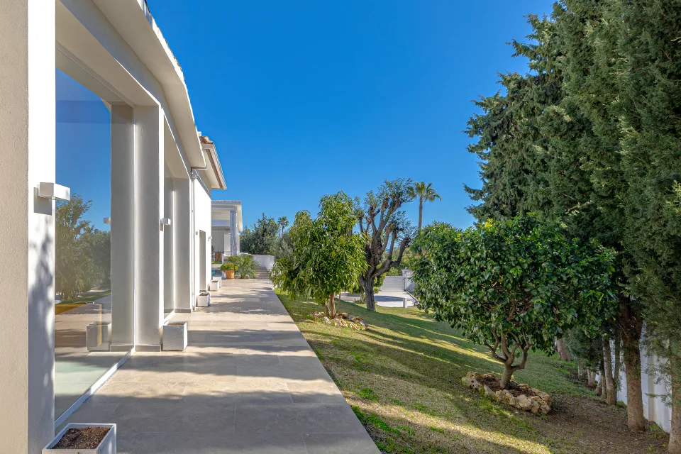 Fotografía inmobiliaria de un amplio jardín con césped verde y árboles frutales que rodean la villa en Marbella