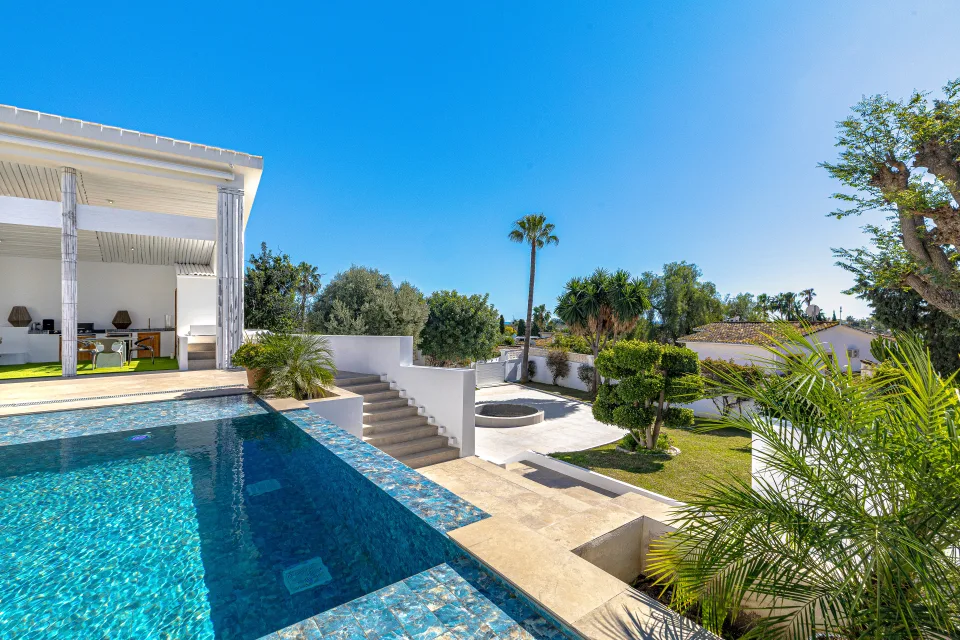 Fotografía inmobiliaria de un exterior con piscina desbordante, jardines bien cuidados y cielo despejado en Marbella