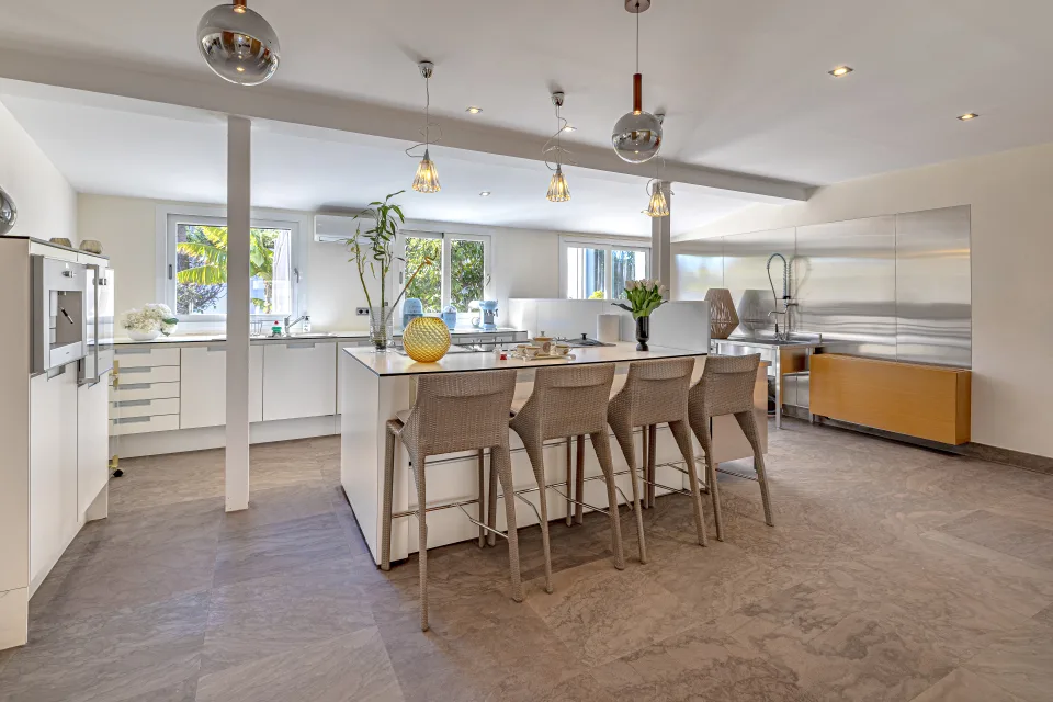 Fotografía inmobiliaria de una moderna cocina con isla central, taburetes de bar y grandes ventanales que aportan luz natural en Marbella