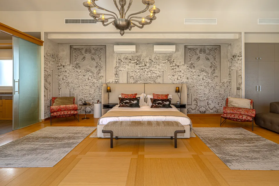 Fotografía inmobiliaria de un elegante dormitorio con cama doble, sillas decorativas y paredes con arte mural en Marbella