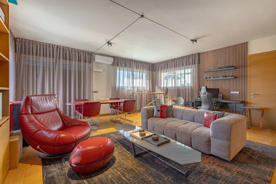 Fotografía inmobiliaria de un salón moderno con sofá claro, sillones rojos, mesa de comedor y luz natural en Marbella