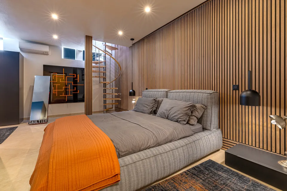 Fotografía inmobiliaria de un dormitorio moderno con paredes de madera, cama grande y escalera spiral en Marbella