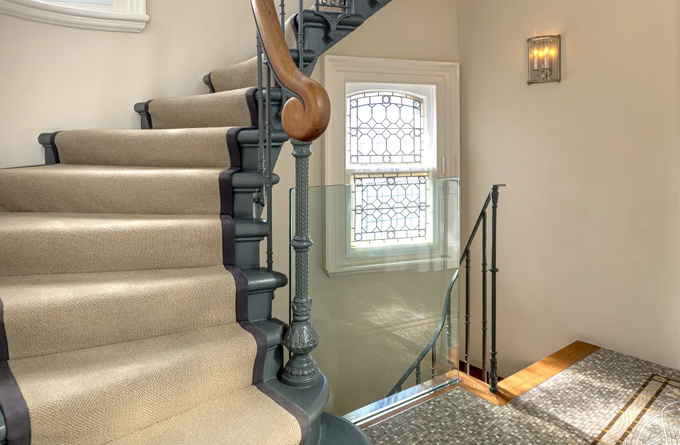 Fotografía inmobiliaria de una escalera elegante con pasamanos de madera y alfombra clara que conduce a un descanso luminoso en Londres