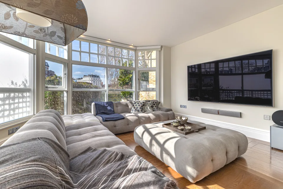 Fotografía inmobiliaria de un luminoso salón con ventanales amplios, sofá esquinero y mesa de centro elegante en Londres