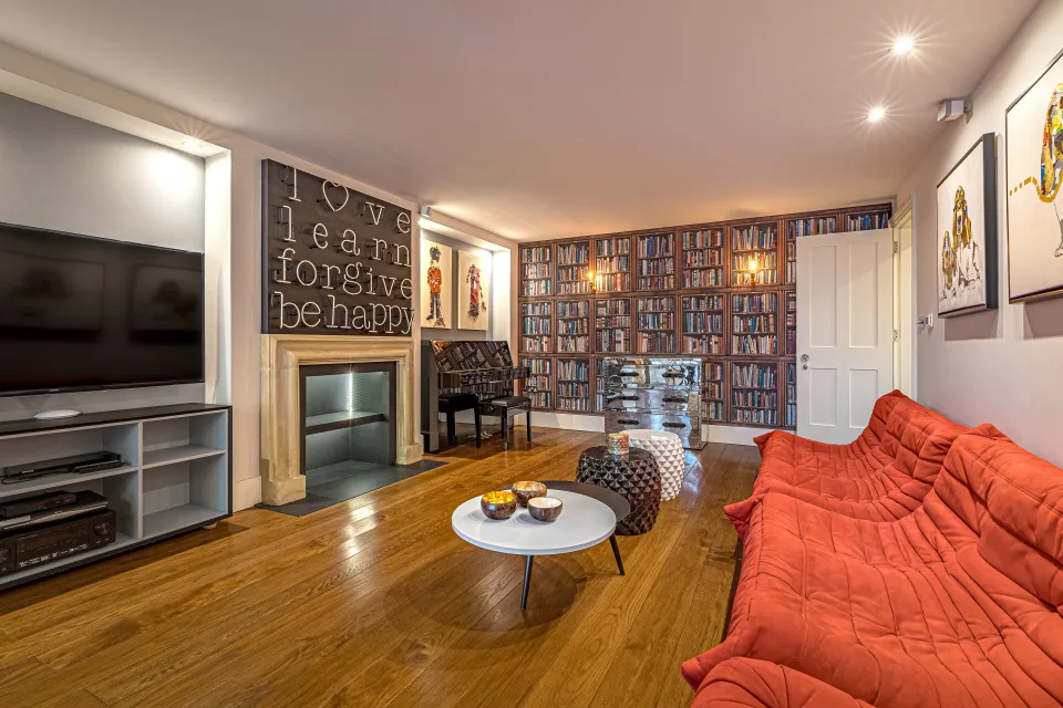 Fotografía inmobiliaria de un salón acogedor con sofá rojo, chimenea moderna y estantería repleta de libros en Londres