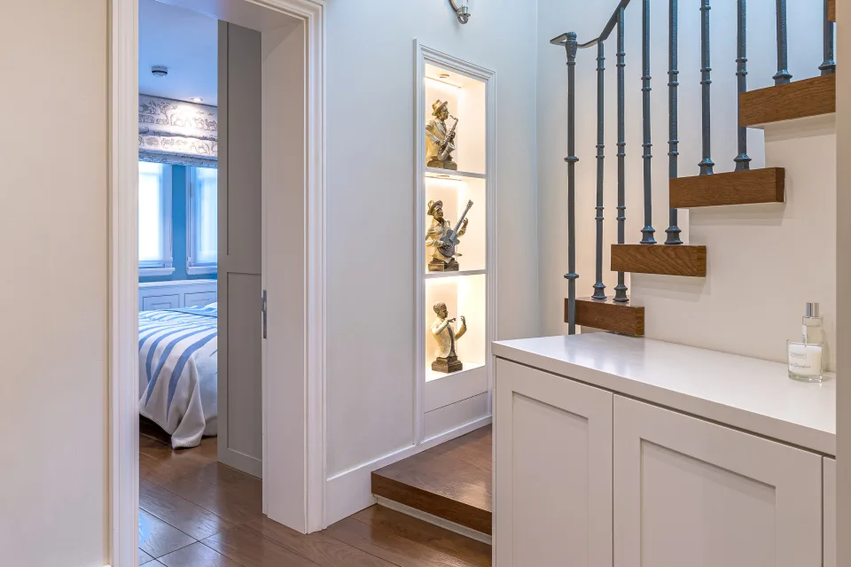 Fotografía inmobiliaria de un pasillo luminoso con escalera de madera y estantería iluminada con esculturas en Londres