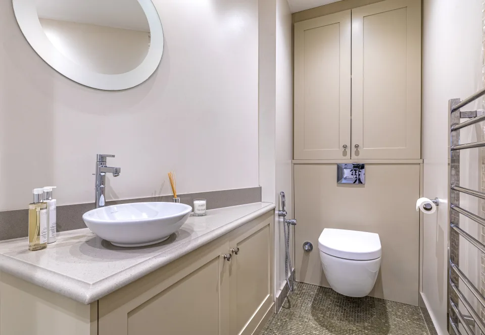 Fotografía inmobiliaria de un elegante baño con lavabo moderno, mobiliario en tonos neutros y detalles en acero inoxidable en Londres