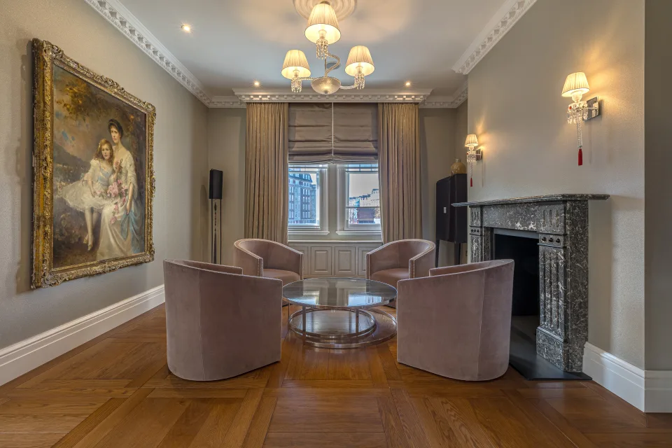Fotografía inmobiliaria de un salón elegante con cuatro sillones de terciopelo, mesa de cristal y chimenea de mármol en Londres