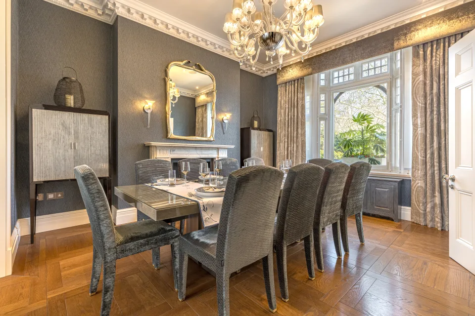 Real estate photograph of an elegant dining room with a glass table, upholstered chairs, and large windows in London