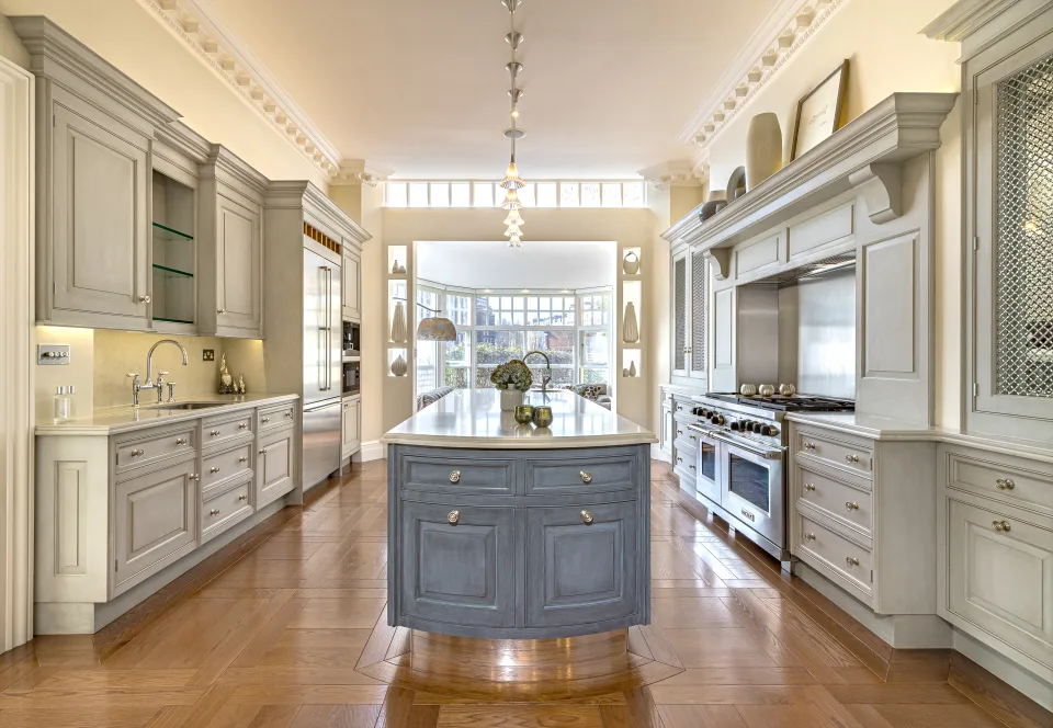 Real estate photograph of a modern kitchen with classic style cabinets, central island with extractor hood and ample natural light in London