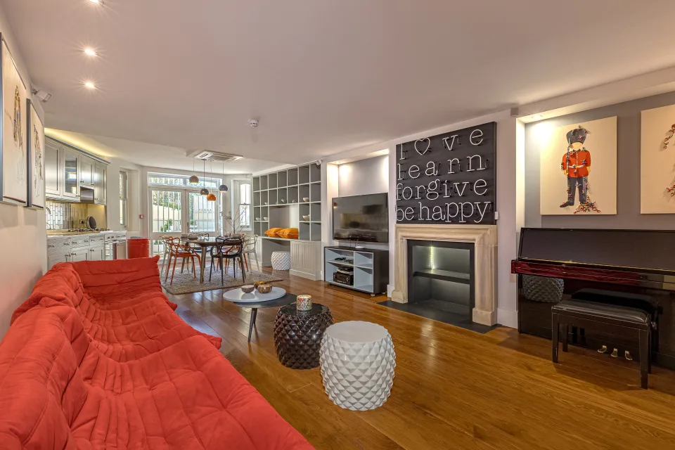 Real estate photograph of a modern living room with a red sofa, circular coffee table, and artistic decor in London
