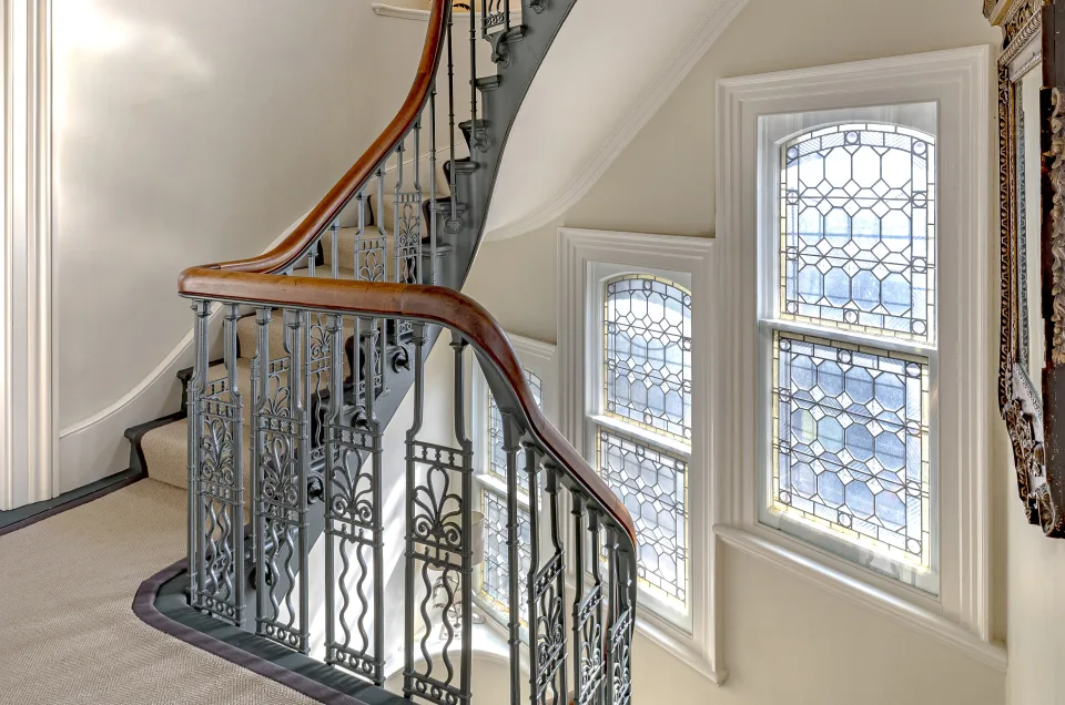 Real estate photograph of a staircase with wrought iron railing, stained glass windows and natural light in London