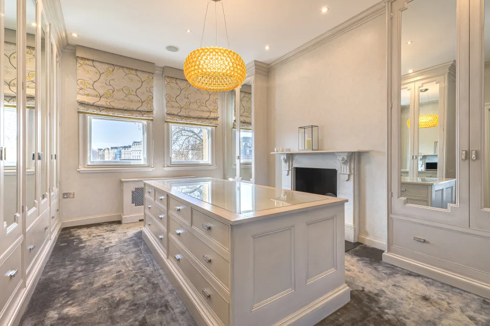 Real estate photograph of a stylish dressing room with fitted wardrobes, central island and natural light in London