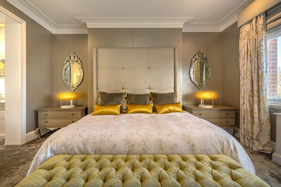 Real estate photograph of an elegant bedroom with a large bed, upholstered headboard and golden table lamps in London