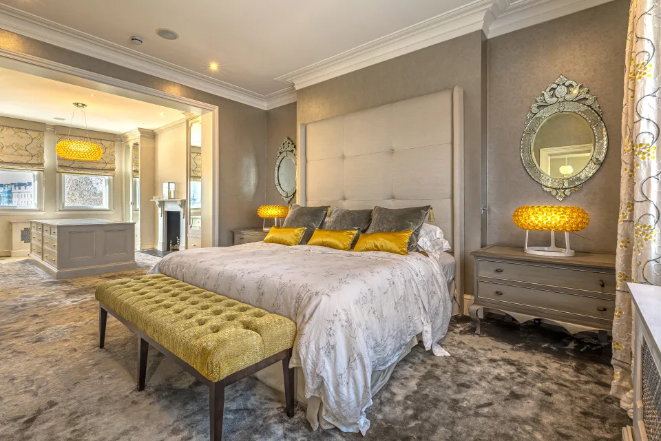 Real estate photograph of a stylish bedroom with a large bed, upholstered headboard and yellow lamps in London