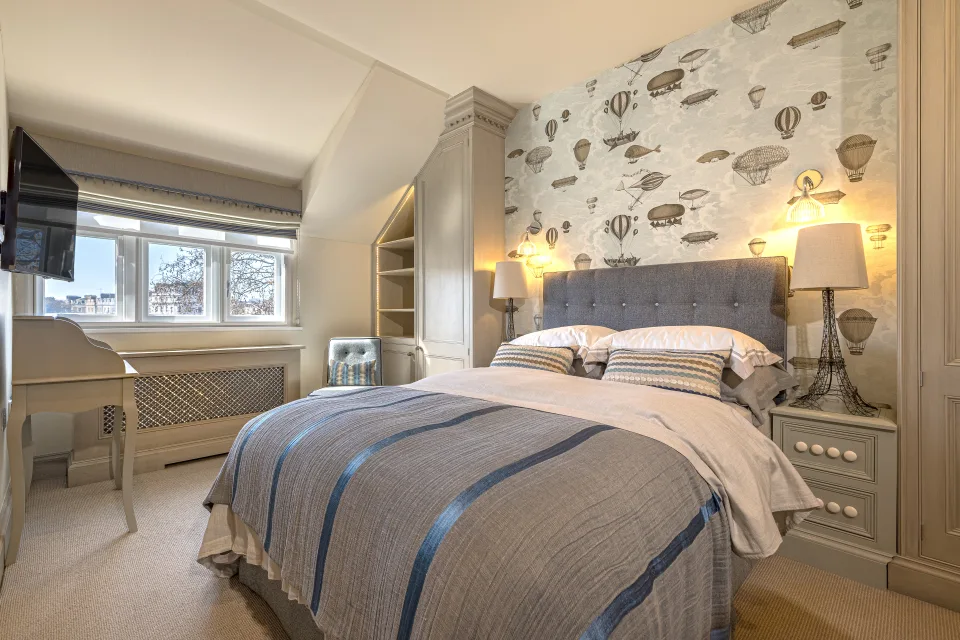 Real estate photograph of a cosy bedroom with upholstered headboard, bedside tables and bright windows in London