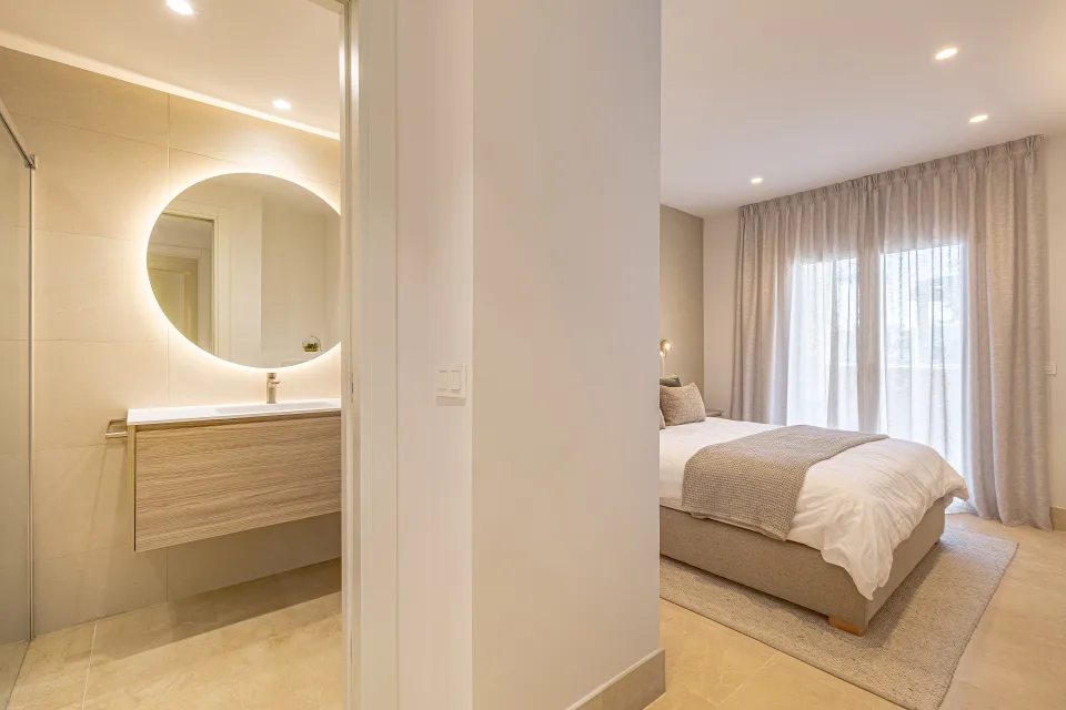 Fotografía de interiorismo y arquitectura de un elegante dormitorio con cama doble, luz natural y baño contiguo en Sotogrande