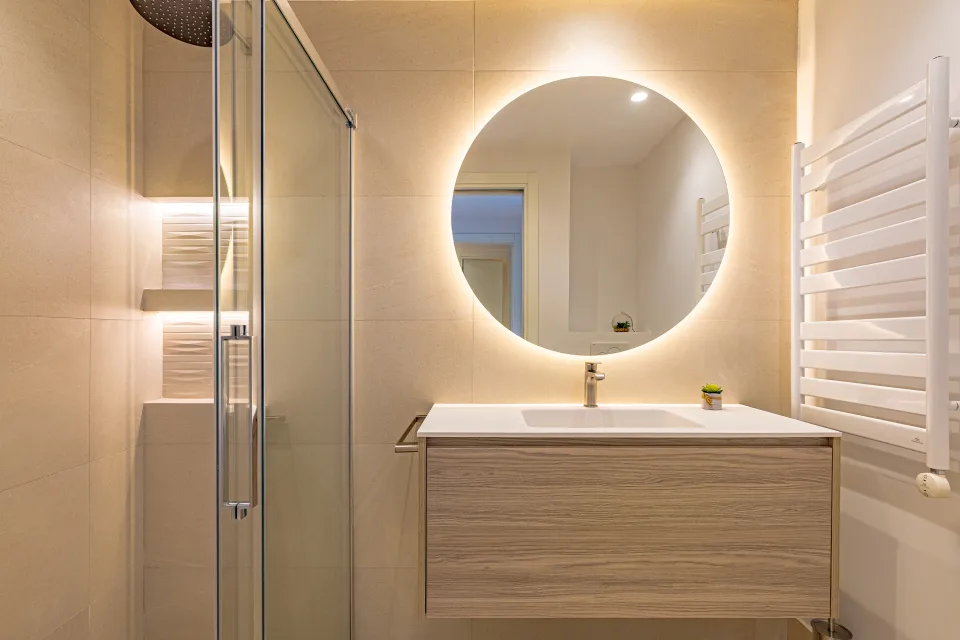 Fotografía de interiorismo y arquitectura de un baño moderno con ducha, lavabo suspendido y espejo redondo iluminado en Sotogrande