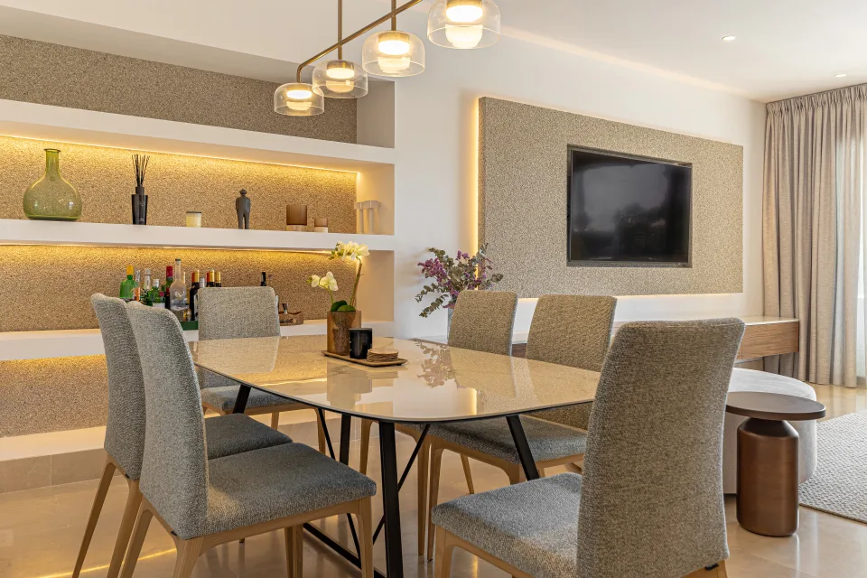Interior design and architecture photograph of a stylish dining room with a glass table, upholstered chairs, and a backlit shelf in Sotogrande