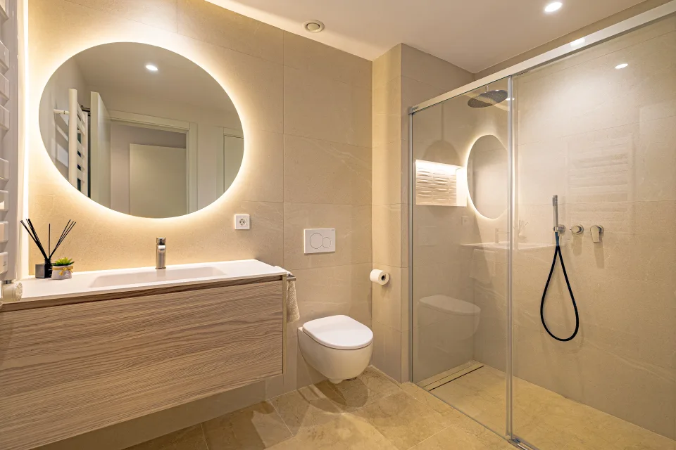 Interior design and architecture photograph of a modern bathroom with walk-in shower, integrated sink and illuminated round mirror in Sotogrande